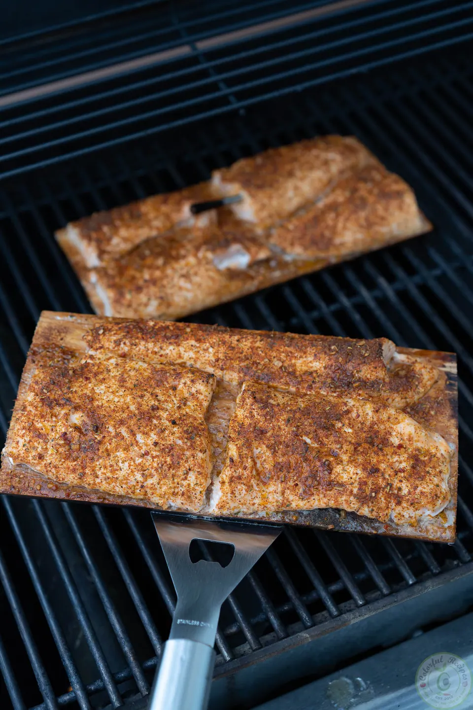 Lifting cedar plank salmon onto the grill with a metal spatula