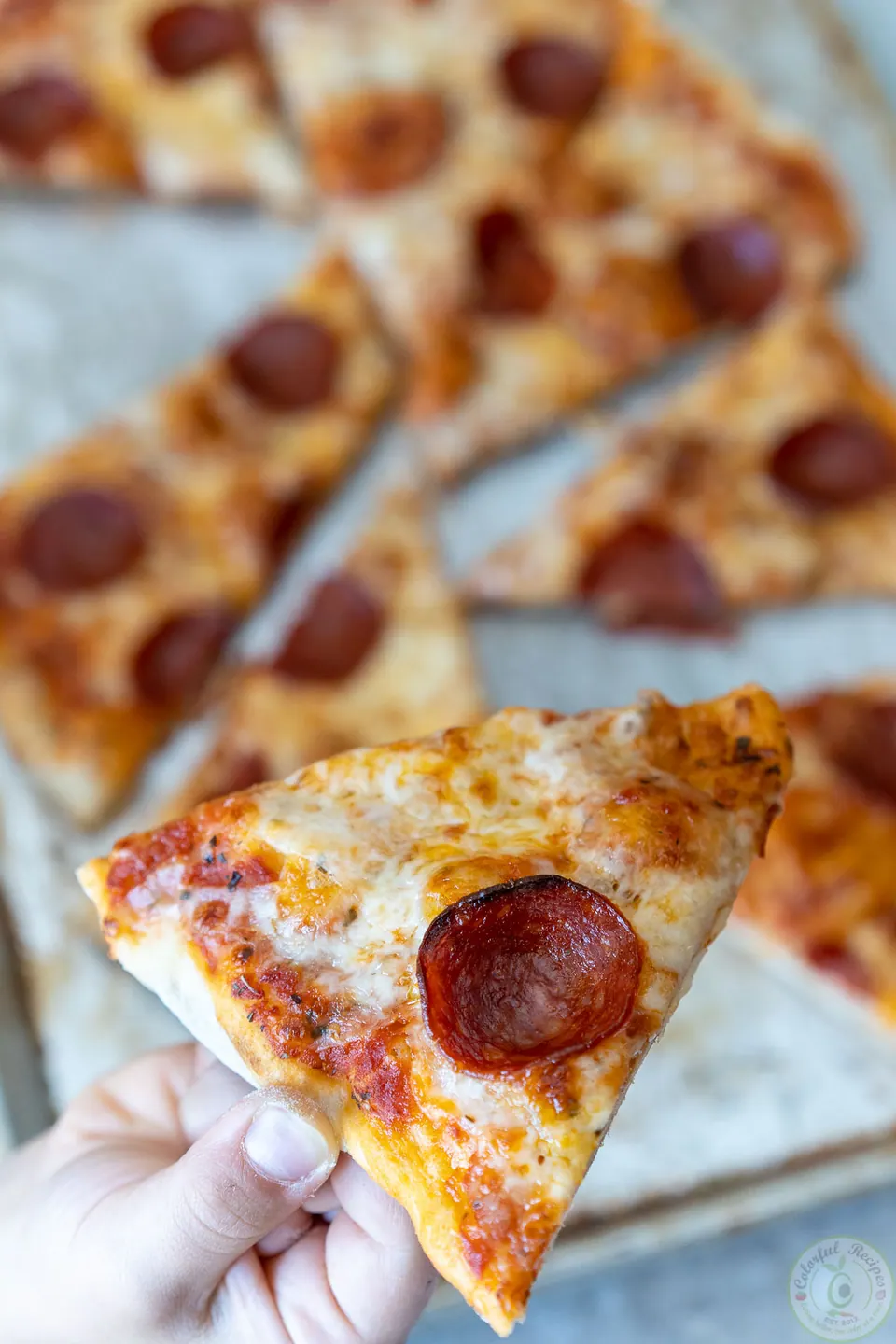 Hand holding a slice of classic pepperoni pizza