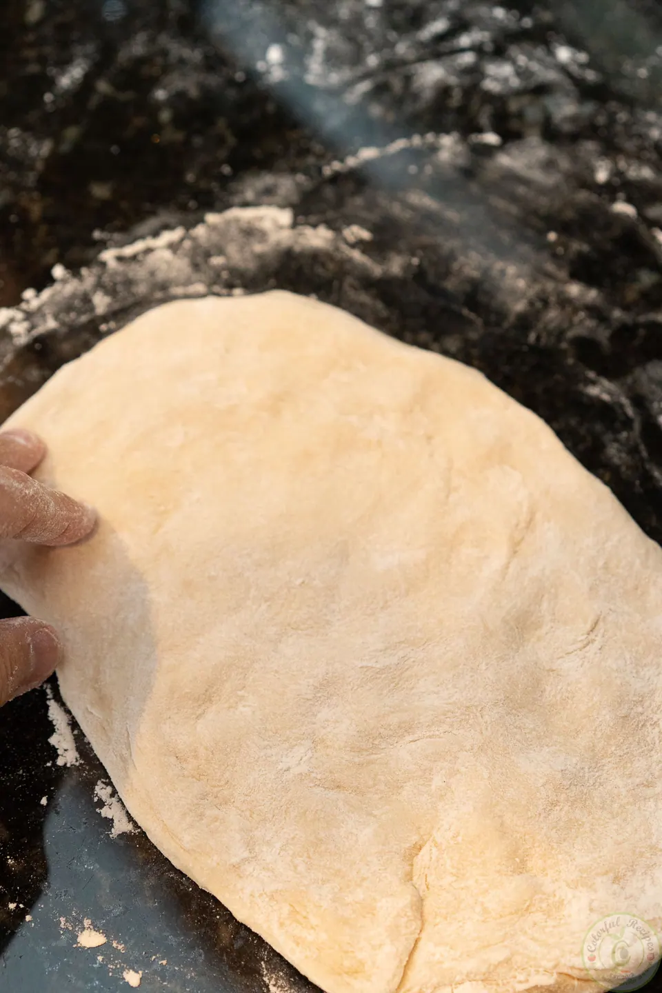 Pressing pizza dough by hand on a floured countertop