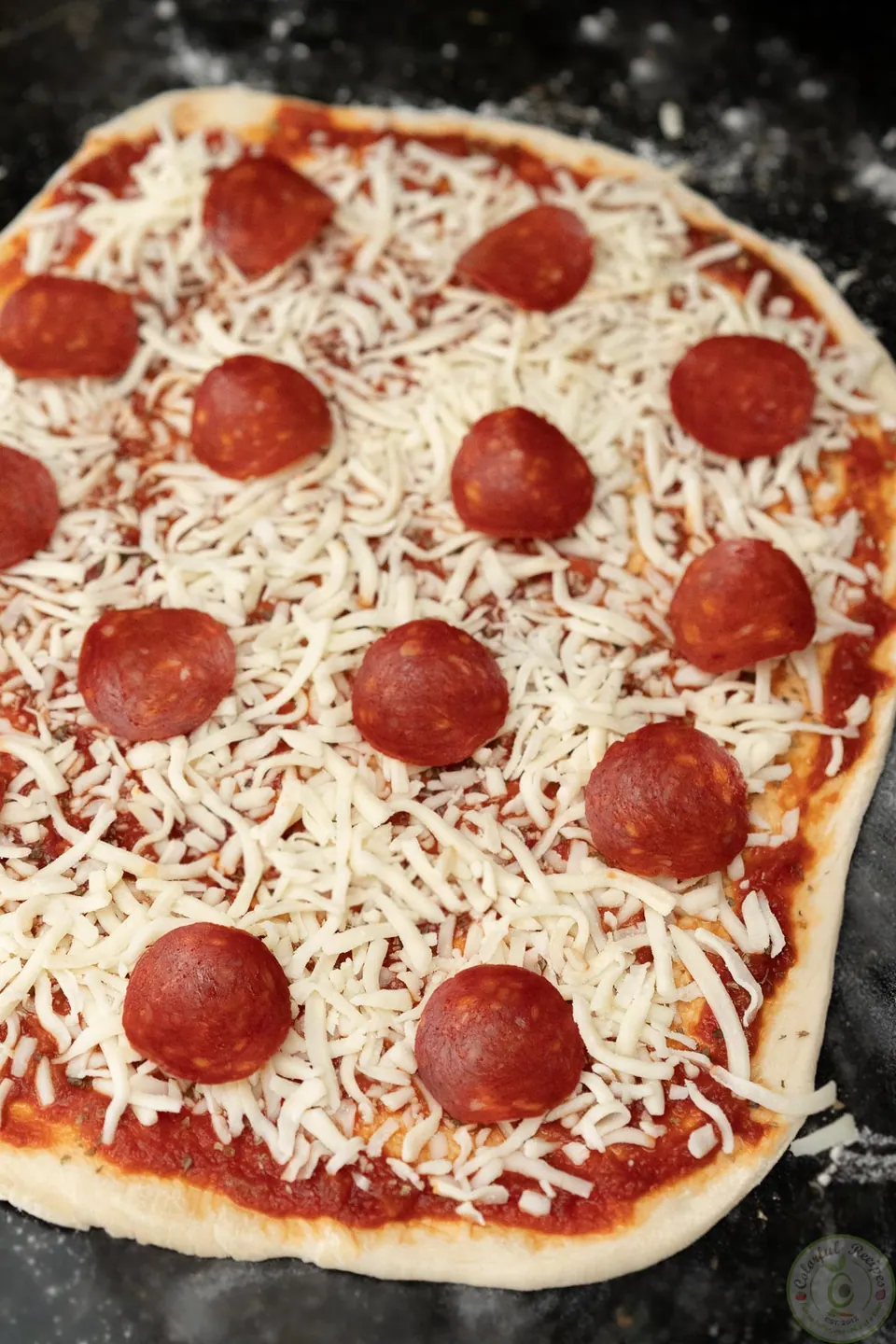 Unbaked pepperoni pizza topped with sauce, shredded mozzarella and pepperoni