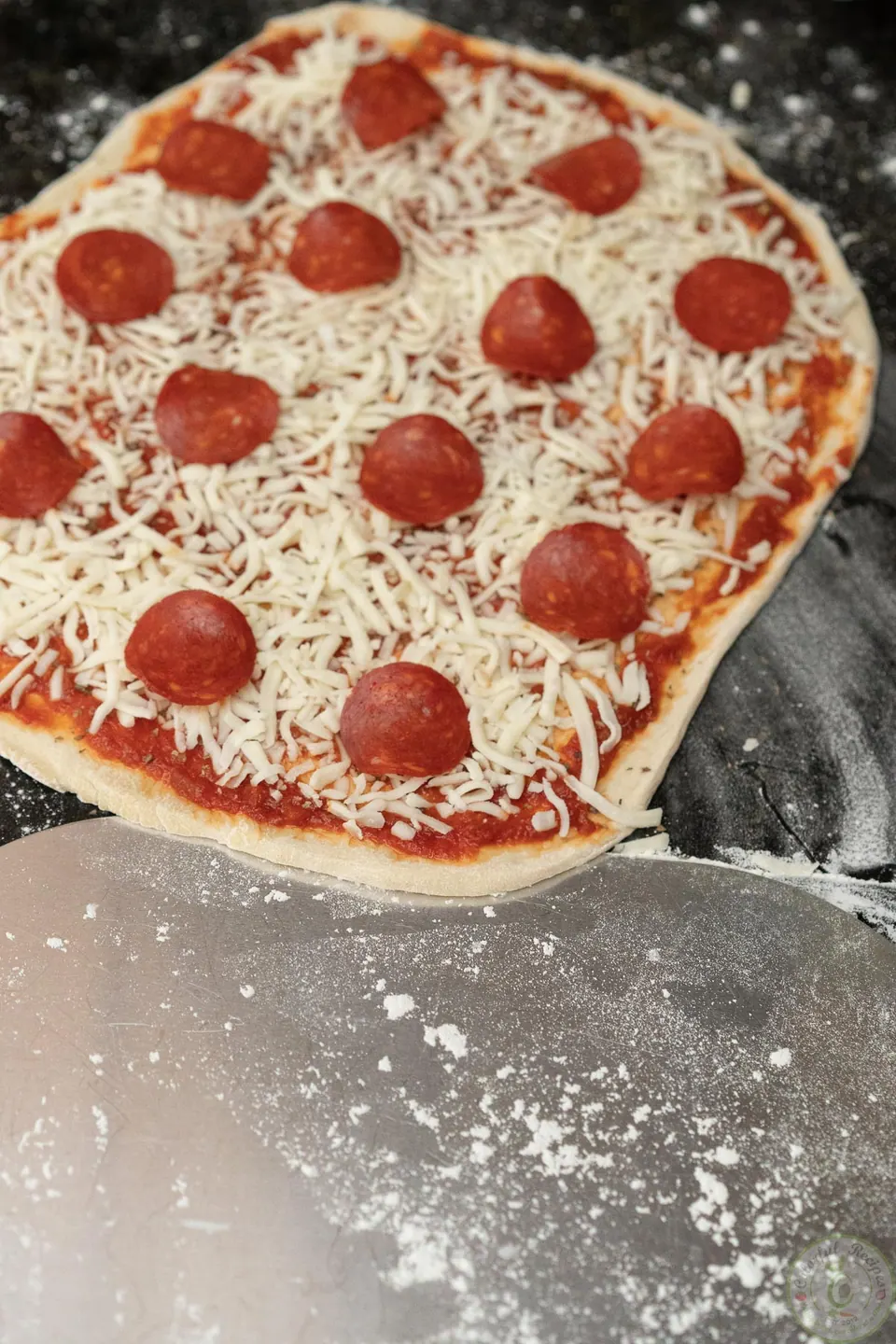 Sliding a floured pizza peel under the unbaked pepperoni pizza