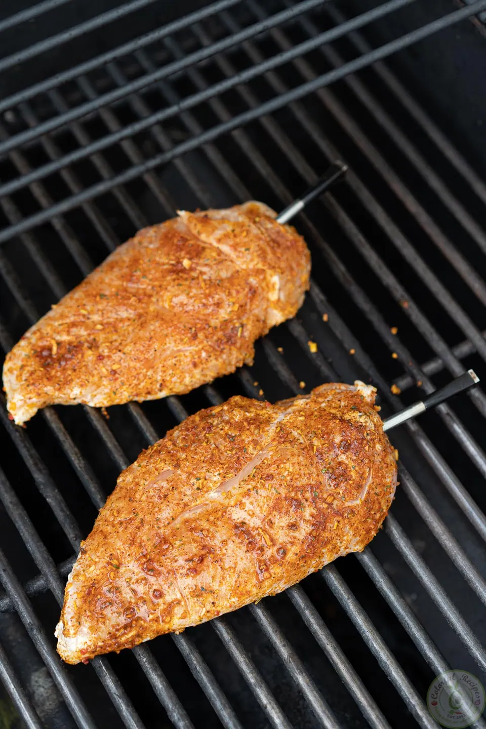 Seasoned chicken breasts with a thermometer probe on the grill
