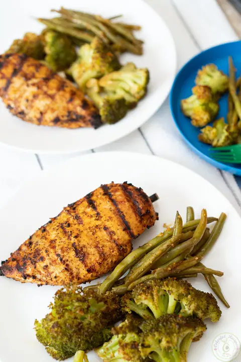 Grilled chicken breast with steamed green beans and broccoli on a white plate