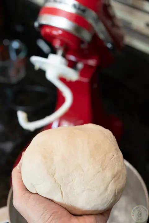 Smooth ball of easy homemade pizza dough held over a stand mixer bowl