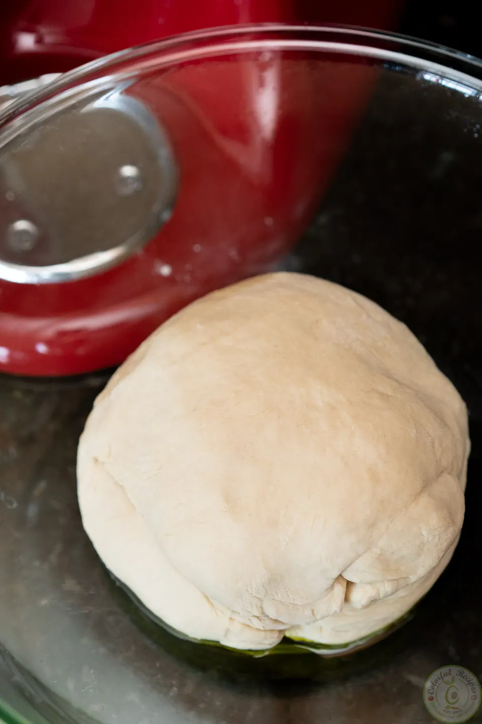 Ball of pizza dough in an oiled glass bowl