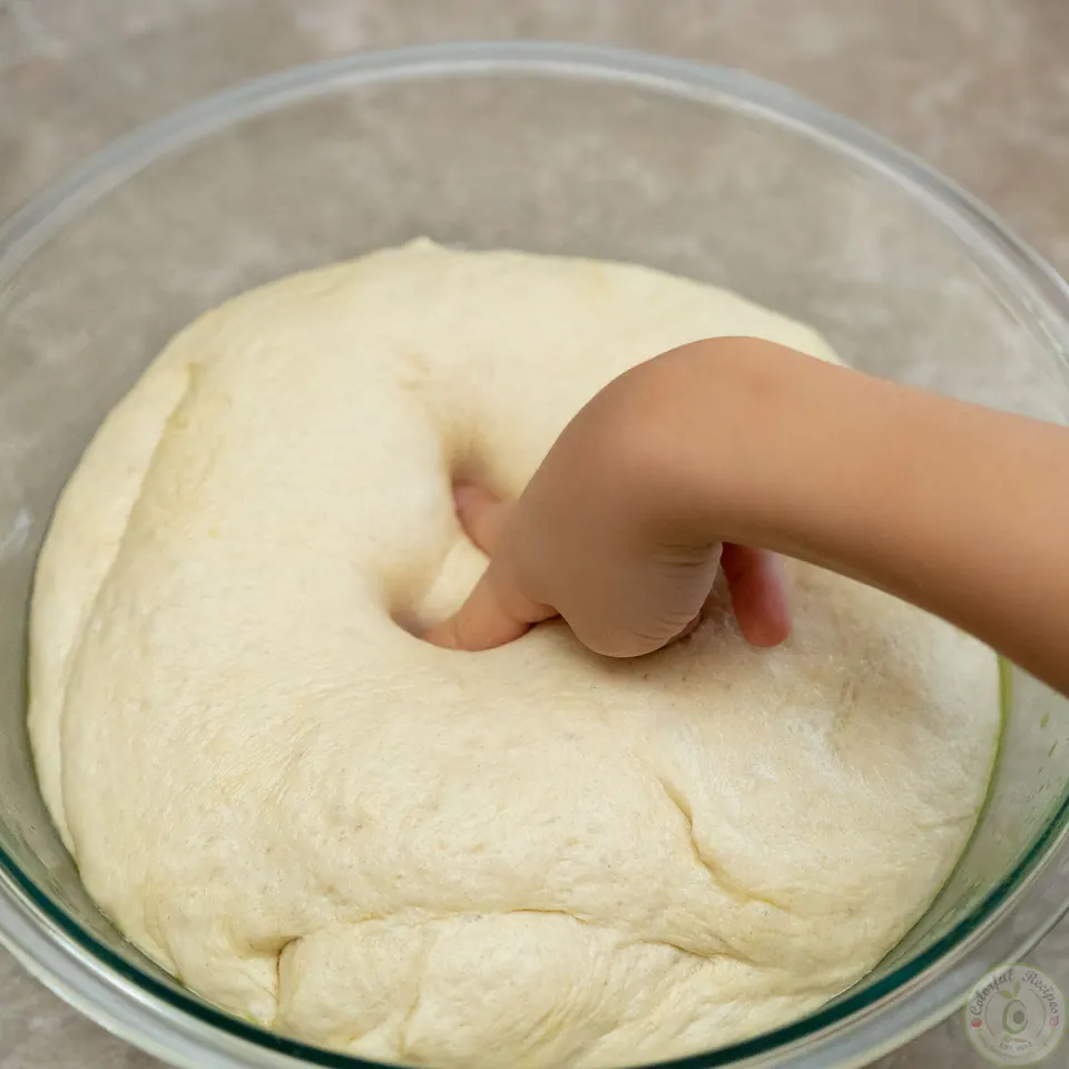 Finger pressing into risen easy pizza dough in a glass bowl
