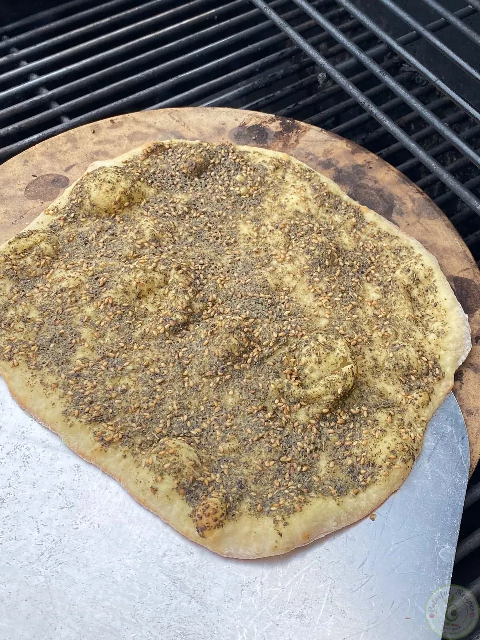 Baked mankousheh being lifted off the pizza stone with a peel
