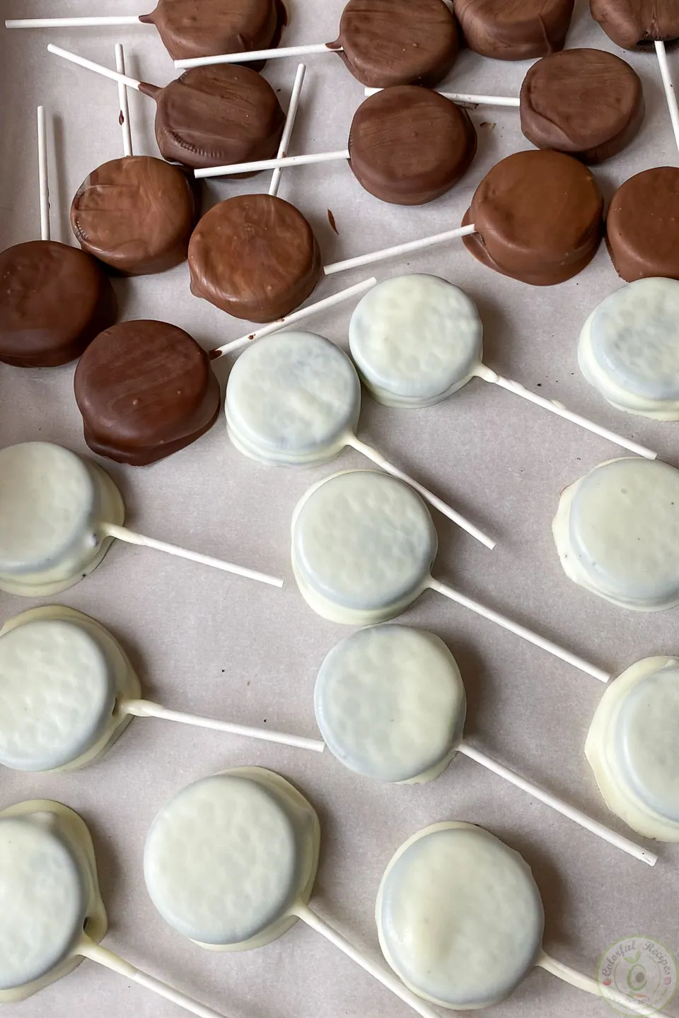 Oreo pops dipped in white and dark chocolate on parchment paper