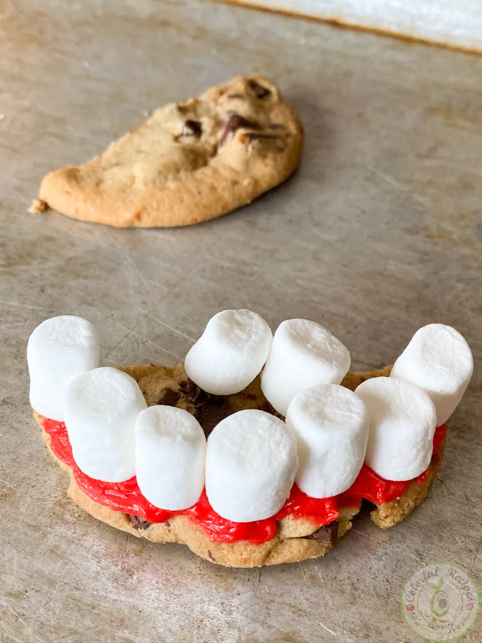 Mini marshmallow teeth pressed into red gel on a cookie half