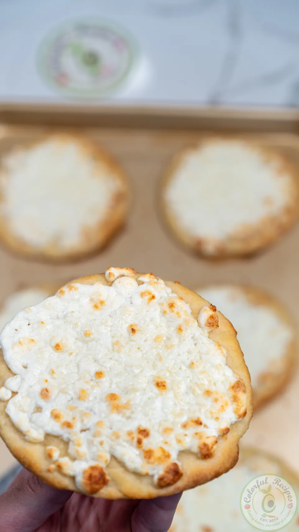 Hand holding a small cheese manakish topped with melted Akkawi cheese